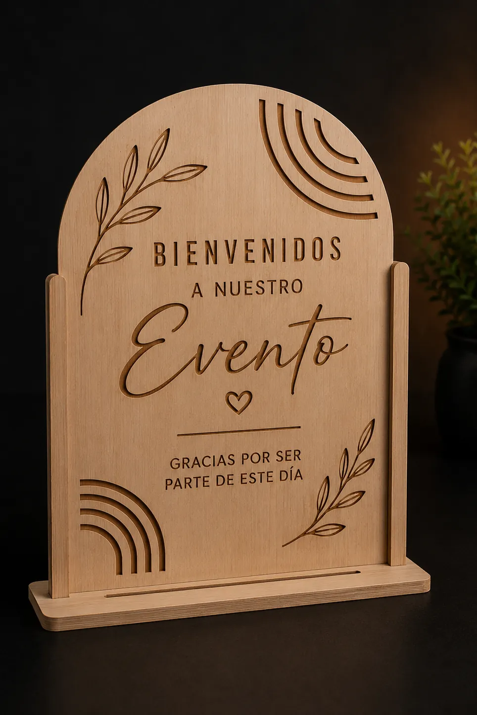 Tablero de madera clara rematado en arco, grabado con la frase "Bienvenidos a nuestro Evento" y ramas de hojas, con arcos concéntricos calados en dos esquinas y encajado en una base plana